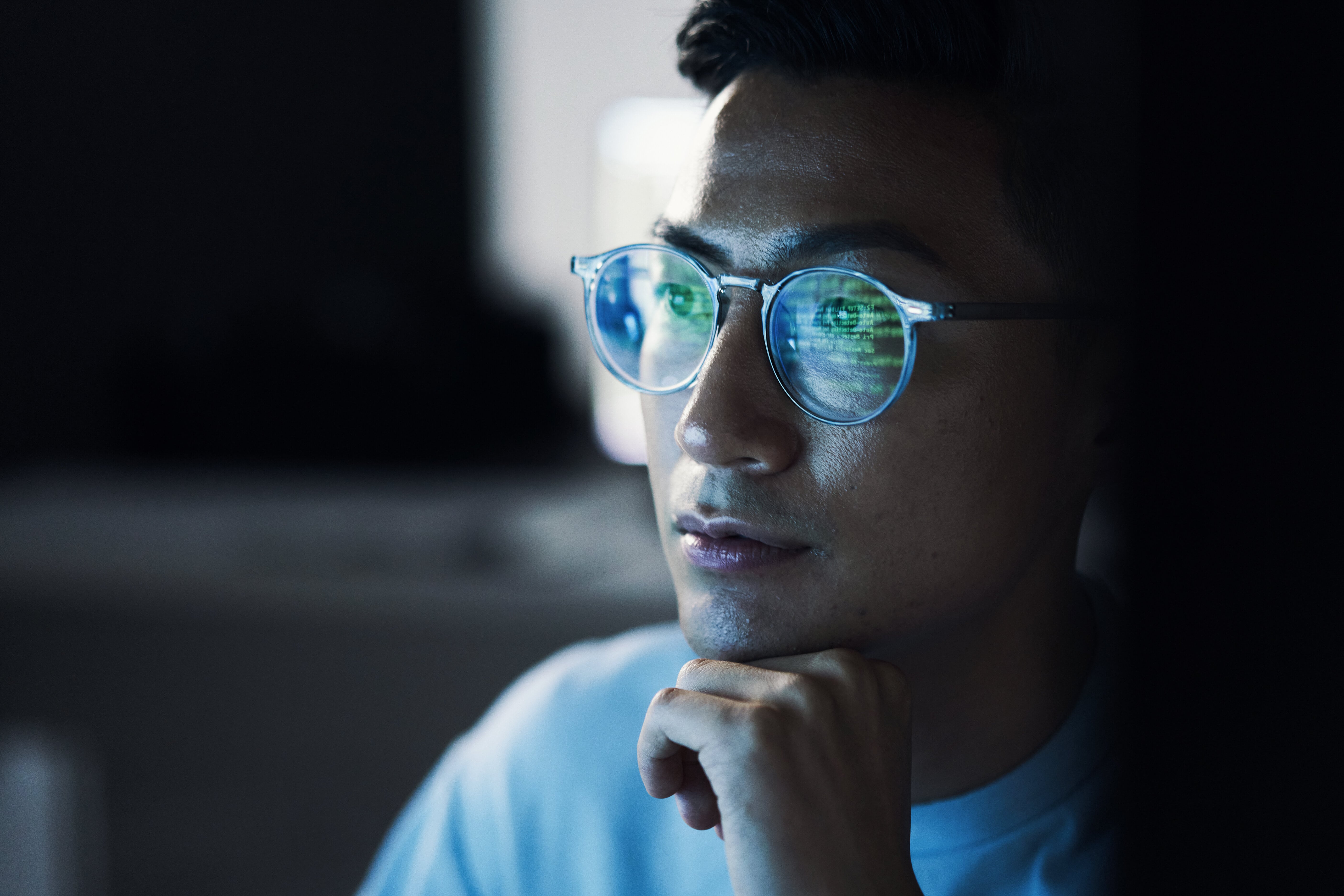Photo d'illustration : Un homme avec des lunettes regarde un écran d'ordinateur hors champ. Les lignes de code présentent sur l'écran se reflètent dans ses lunettes. Valorisation de la donnée. Souveraineté numérique. Numérique.